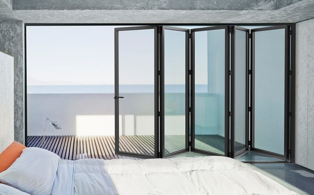 Cortizo black aluminium bi-fold doors opening to a scenic ocean view from a bedroom.