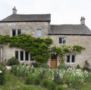 Traditional stone cottage with Alitherm Heritage steel windows, adorned with climbing plants and surrounded by a lush garden.